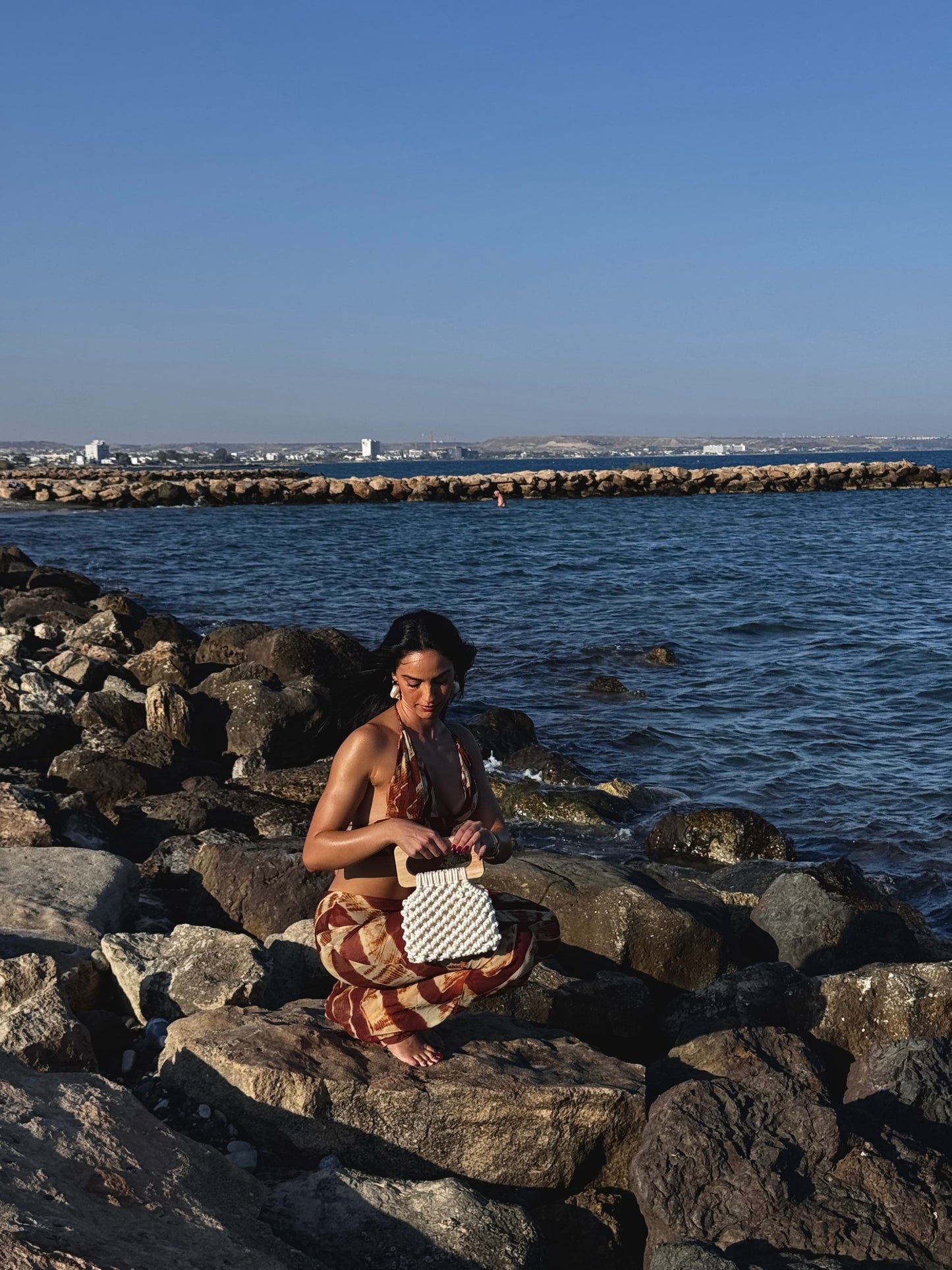 Woman sitting on rocks by the water holding the koma bag