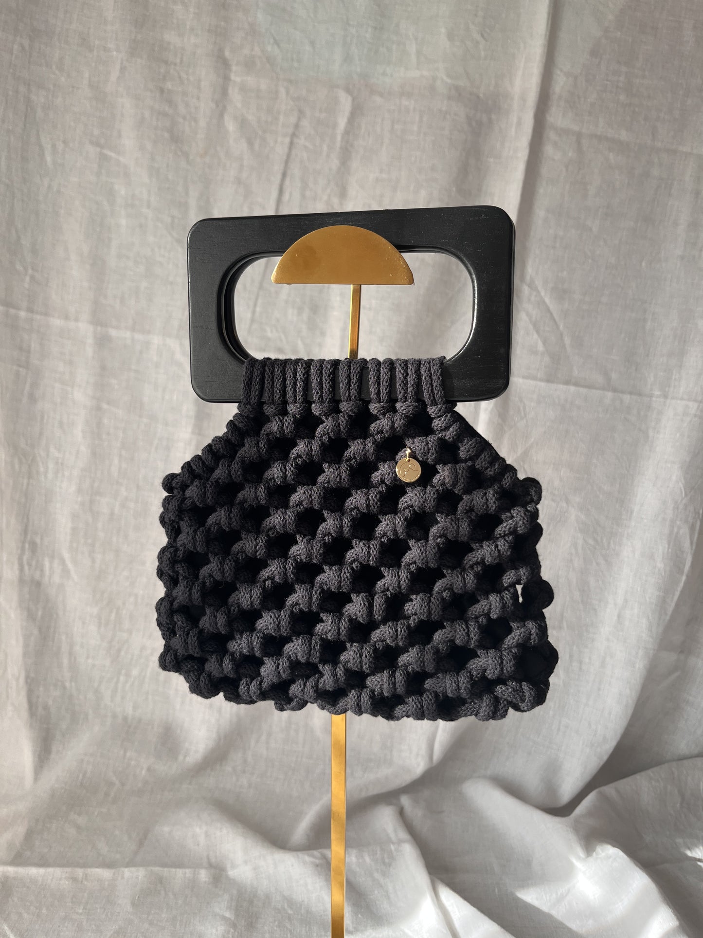Black woven handbag, macrame bag with a wooden handle on a light gray background