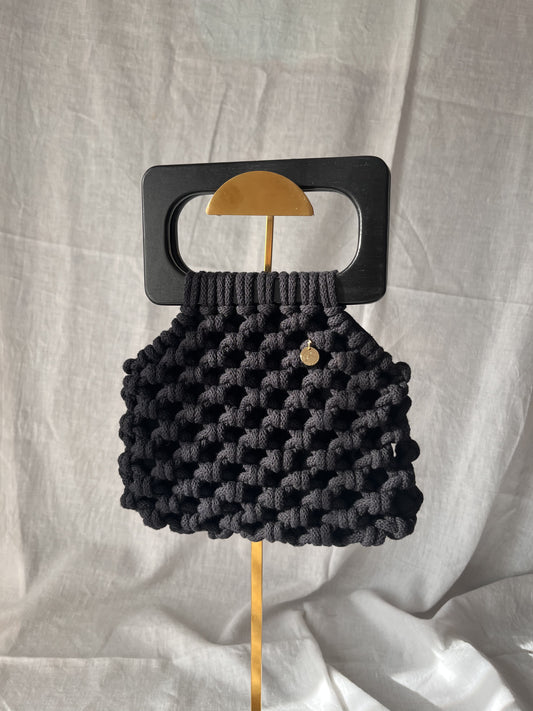 Black woven handbag, macrame bag with a wooden handle on a light gray background