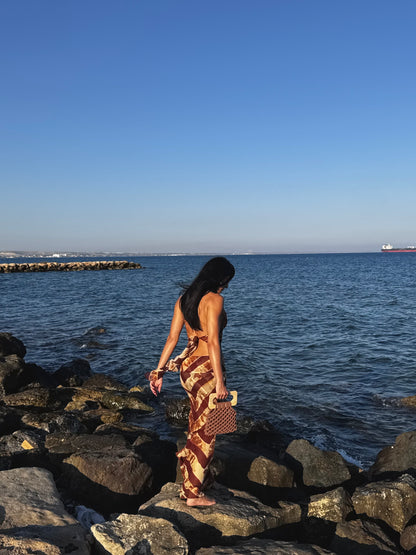 Woman walking along a rocky shoreline with ocean and clear sky in the background WITH THE KOMA BAG