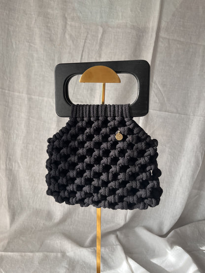 Black woven handbag, macrame bag with a wooden handle on a light gray background
